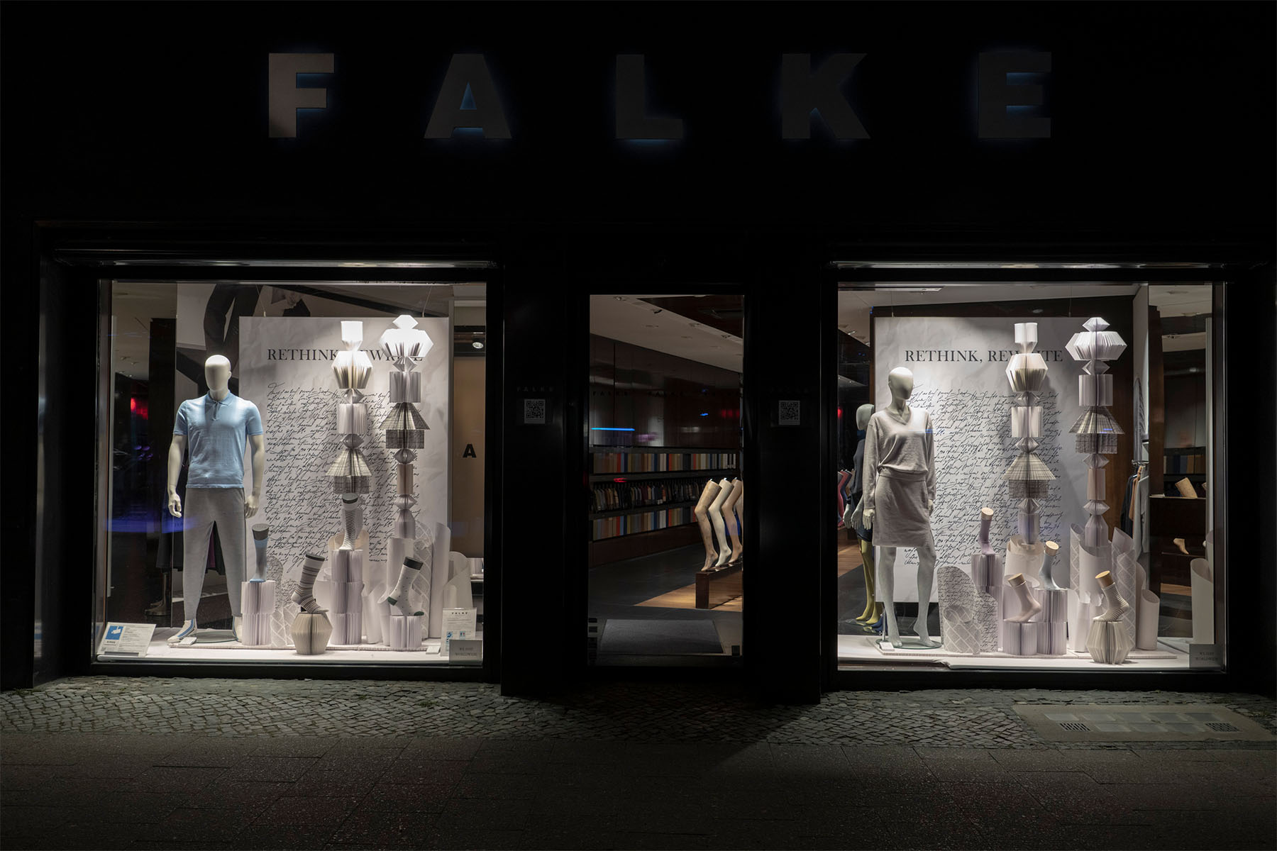 Illuminated FALKE storefront at night with paper sculptures and mannequins for the "Rethink, Rewrite" campaign