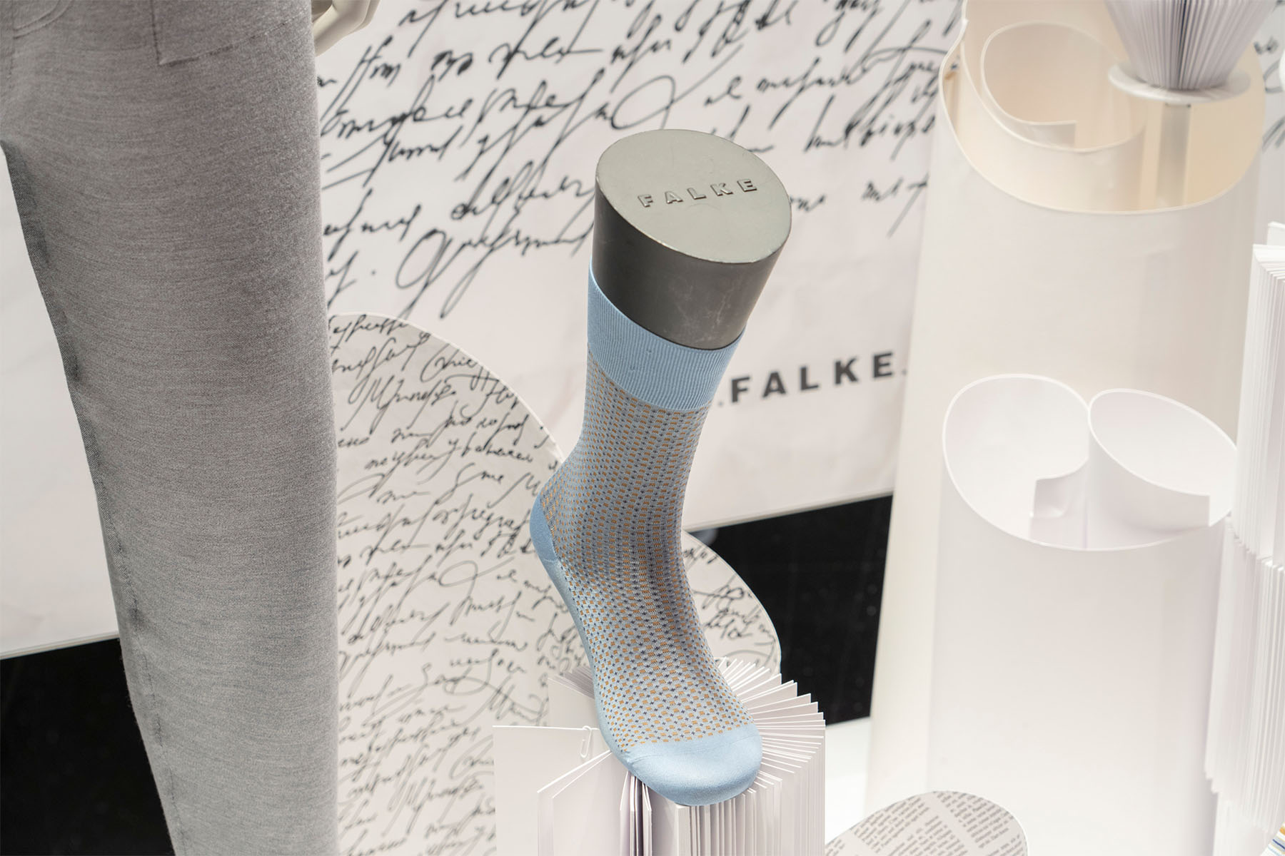 Close-up of a striped FALKE sock on a mannequin foot against handwriting and white paper sculptures
