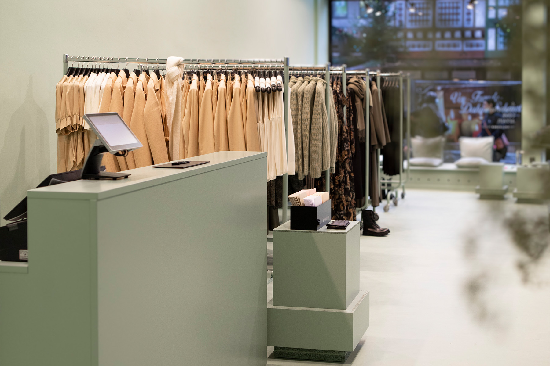 Kassenbereich und Kleiderstangen im lindgrünen Hallhuber-Store mit Blick zur Straße