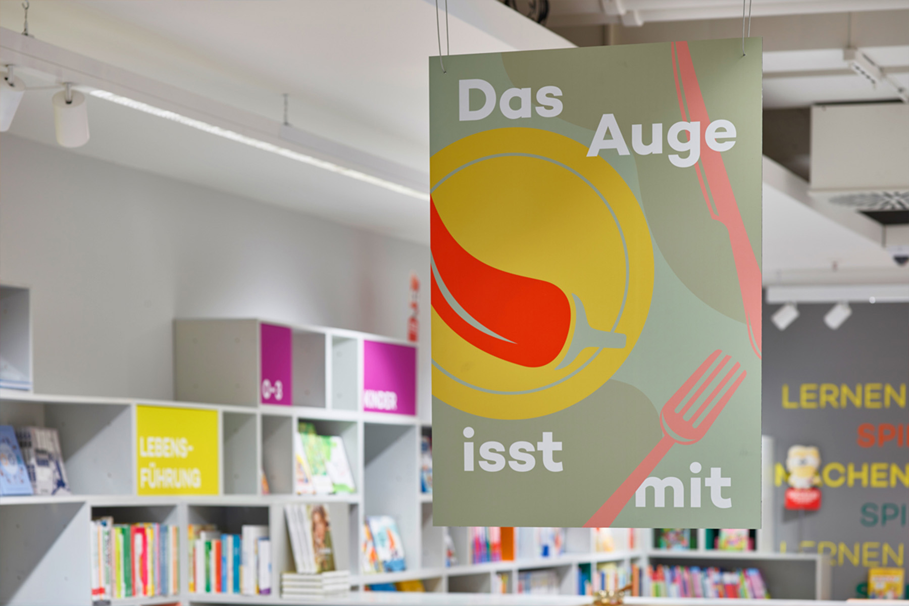 Hanging sign "Das Auge isst mit" with a plate illustration above the cookbook shelves at Hugendubel.