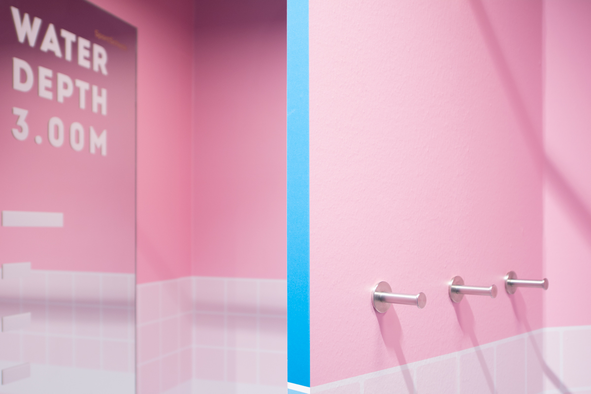 Rosa Umkleidekabine mit Spiegel „Water Depth 3.00M" und Kleiderhaken an der Wand.