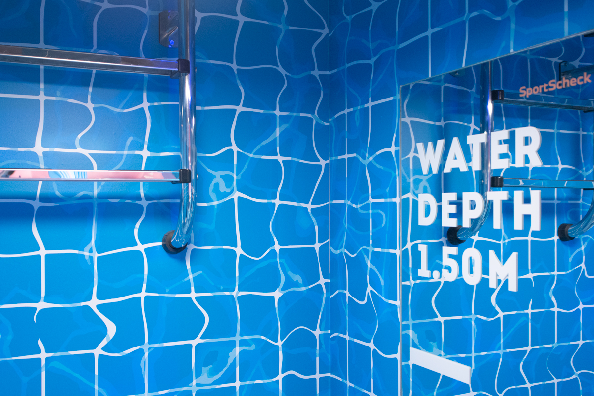 SportScheck-Umkleidekabine mit Pool-Kachel-Optik und Spiegeltext „Water Depth 1.50M".