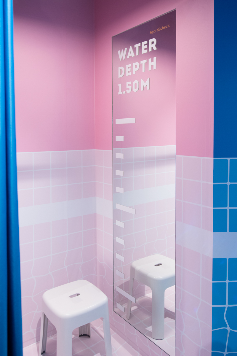 Rosa Umkleidekabine mit Wasserstand-Skala „Water Depth 1.50M" am Spiegel und Hocker.