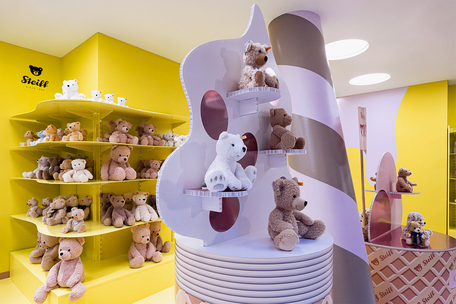 Weiße Eiswaffel-Regale mit Teddybären in runden Nischen vor gelber Wand mit Steiff-Logo