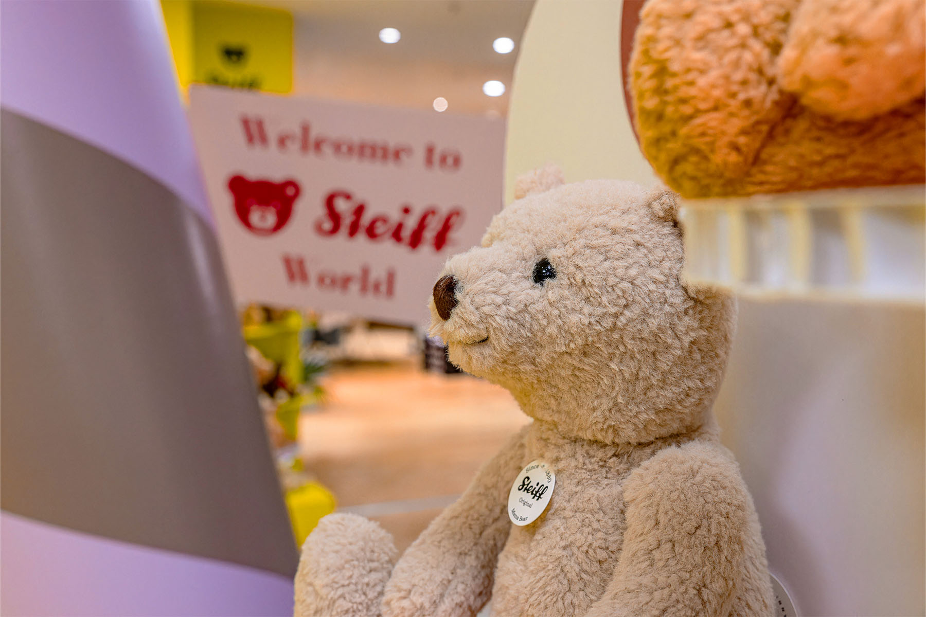 Nahaufnahme eines Steiff-Teddybären mit Knopf im Ohr vor dem „Welcome to Steiff World“-Schild