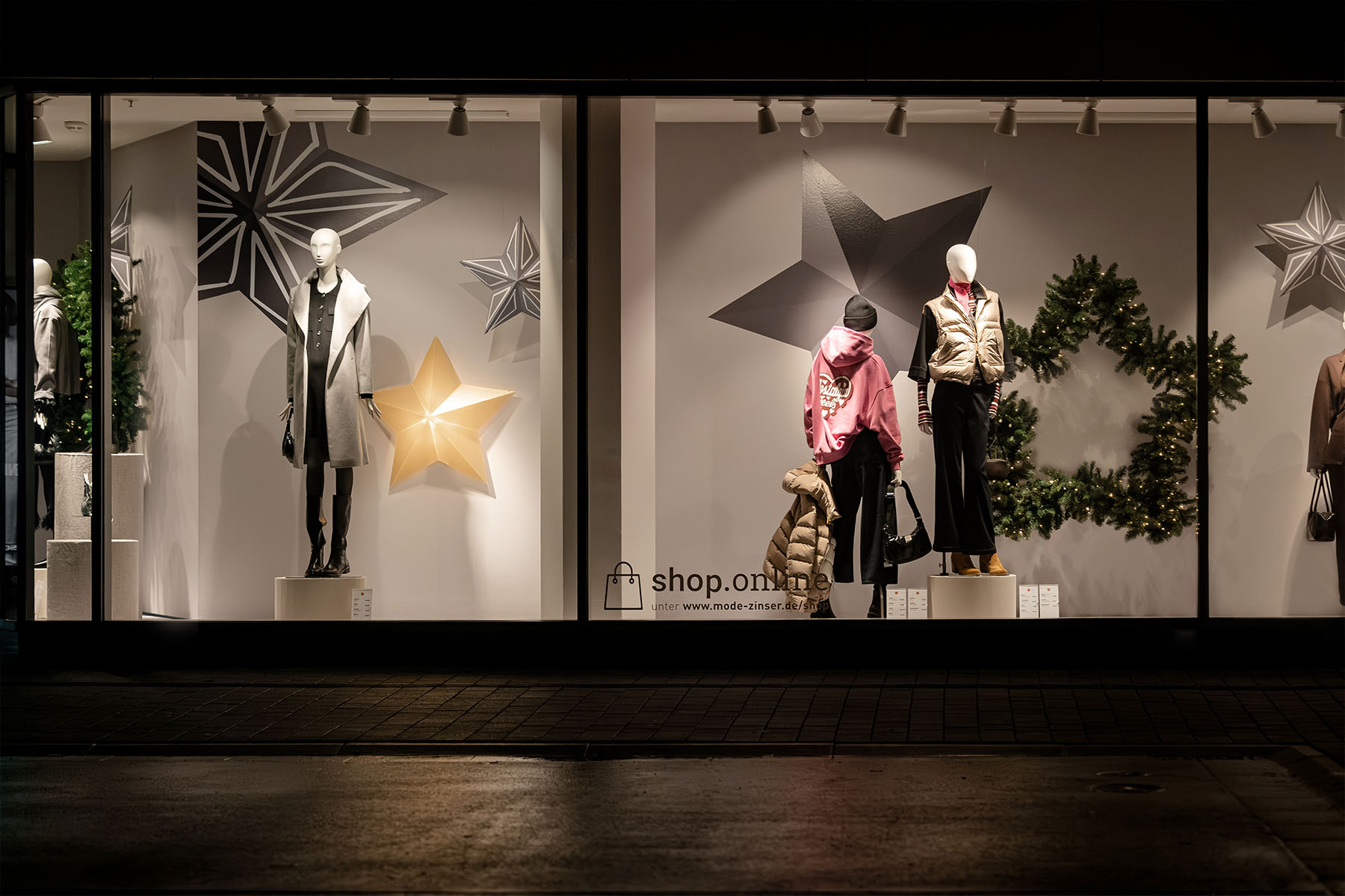 Zinser-Schaufenster bei Nacht mit Mannequins, grafischen Sternen und Tannenkranz.