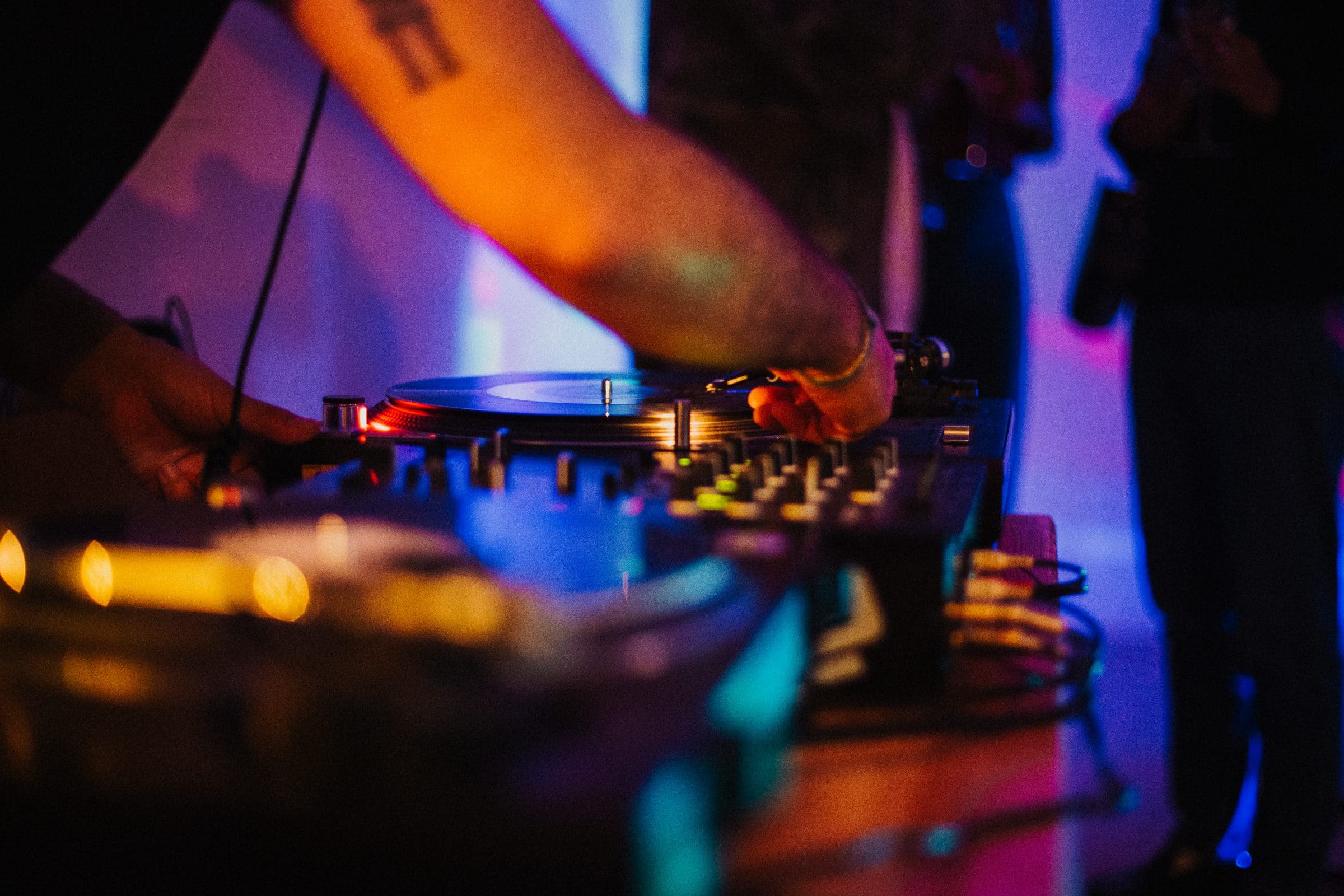 A DJ’s hands on the mixer under colourful club lighting