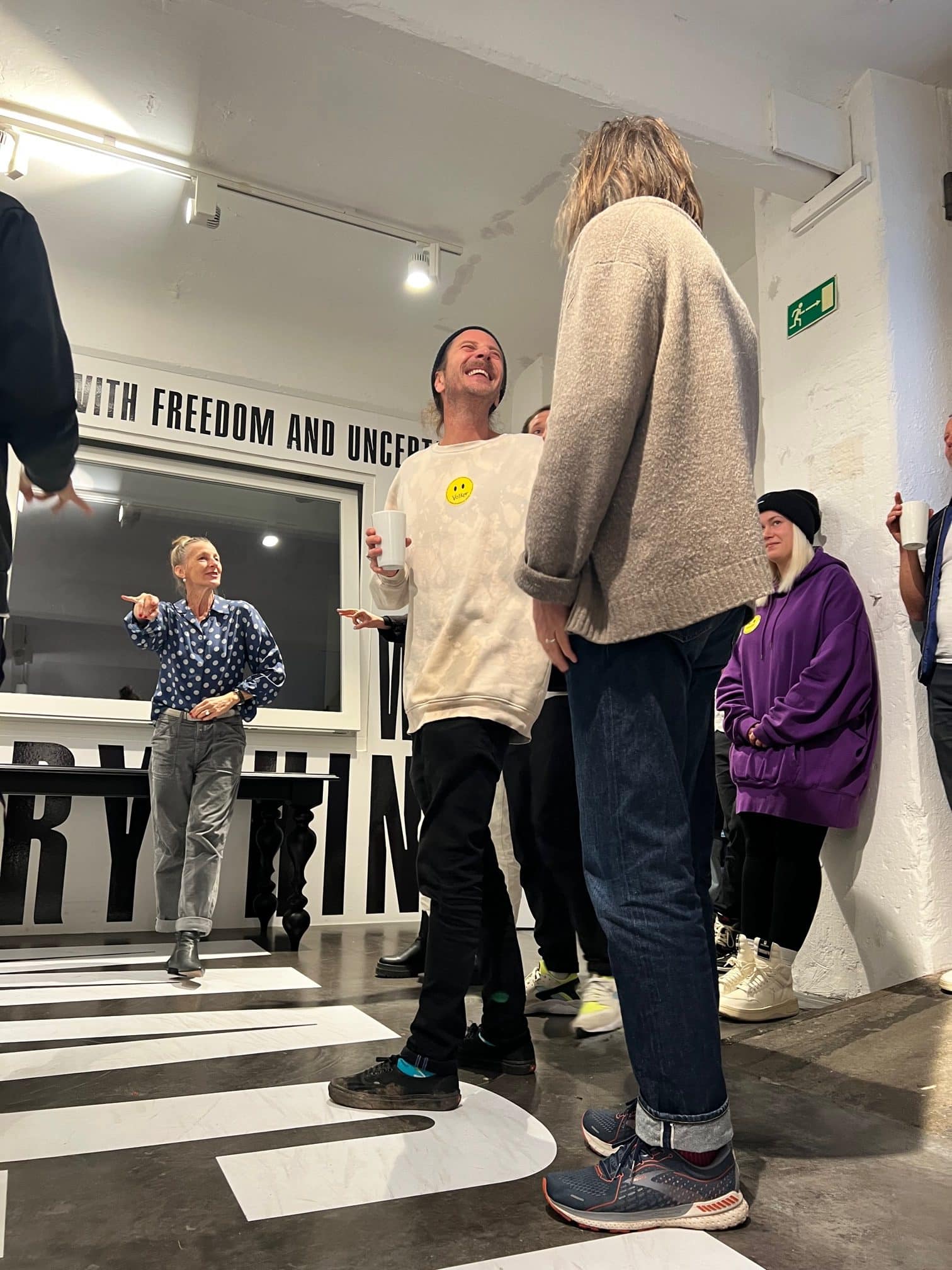 Designplus team laughing in front of a wall lettered about freedom and uncertainty during the workshop
