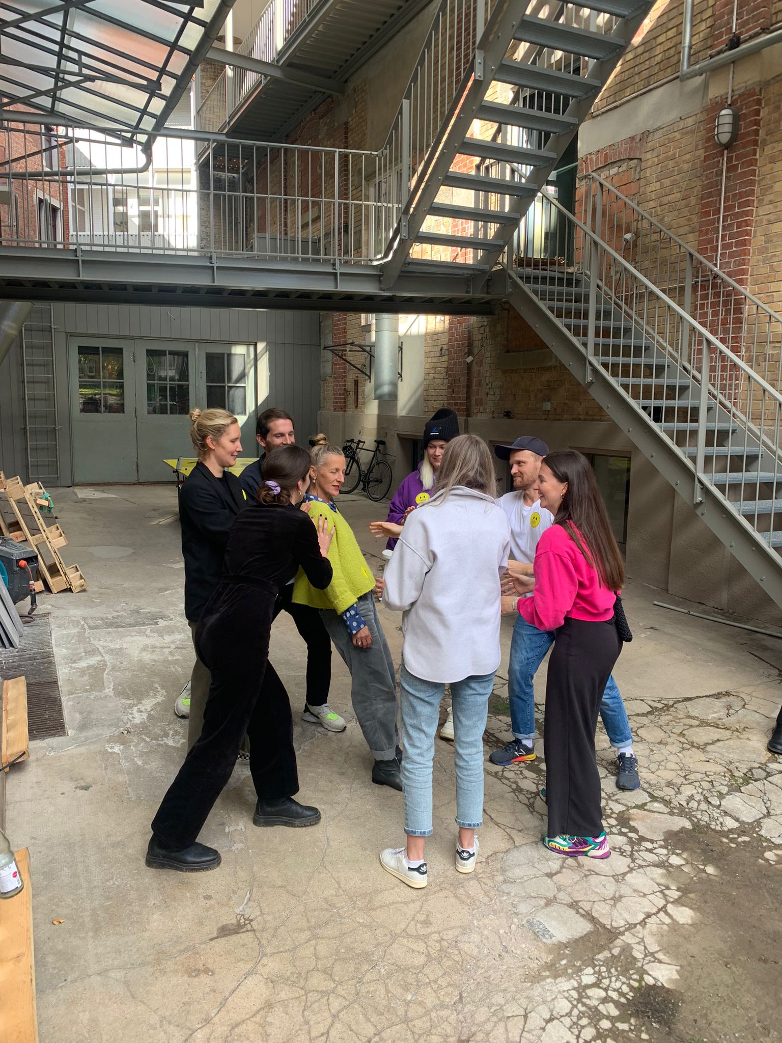 Designplus team standing in a circle in the courtyard during a workshop exercise