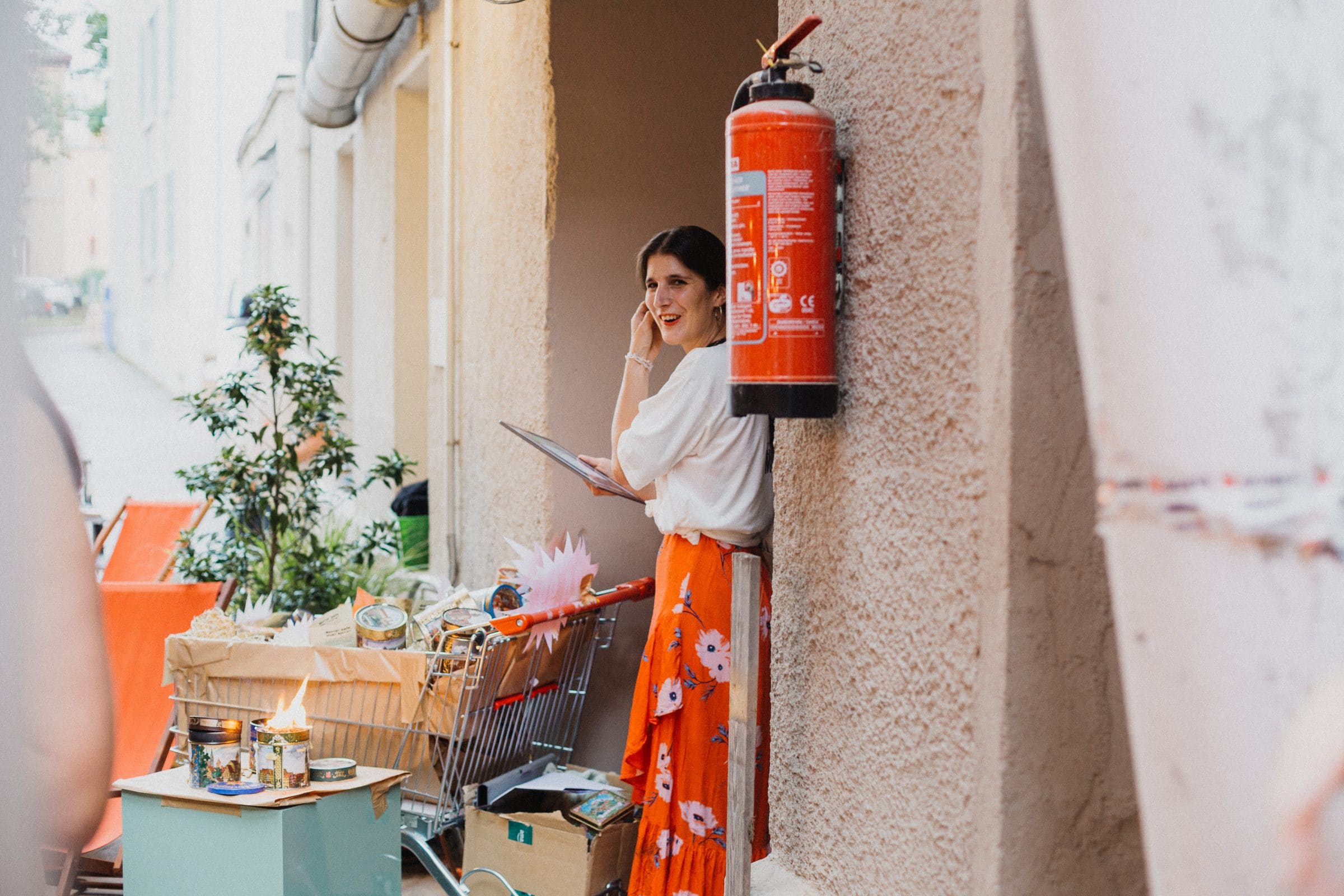 Woman on the phone next to a shopping trolley and fire extinguisher outside Der Super-Markt