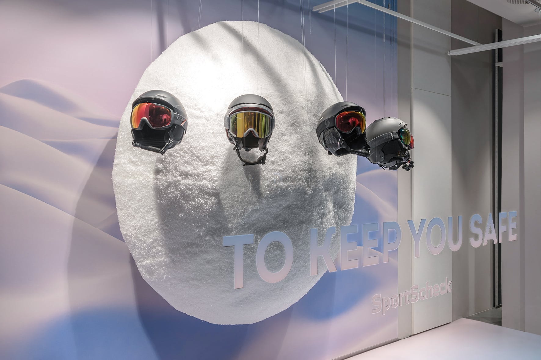 SportScheck-Schaufenster mit Skihelmen und -brillen an schneebedeckter Kugel