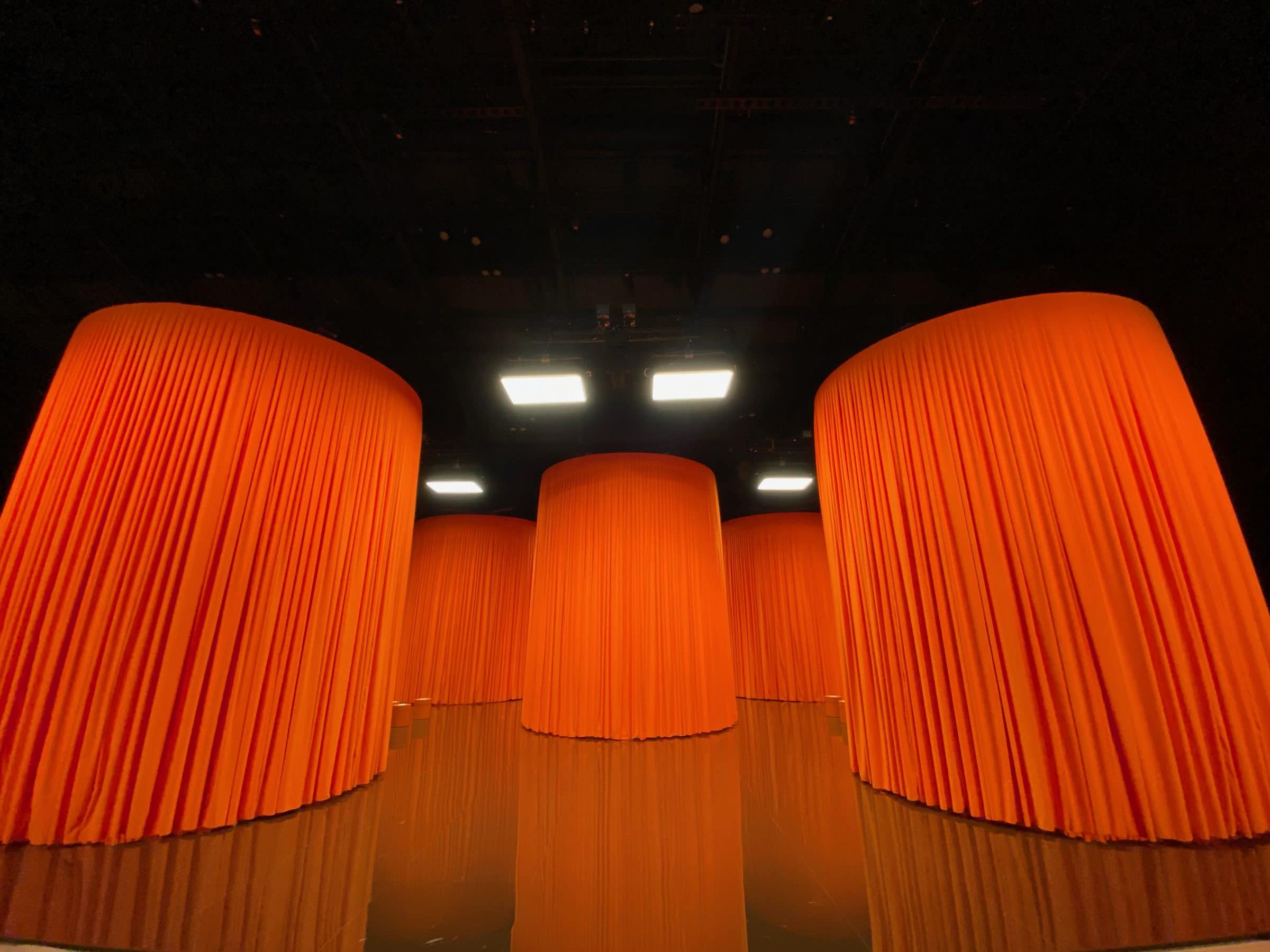 Tall draped orange fabric cylinders forming the Hermès show set, reflected in the floor