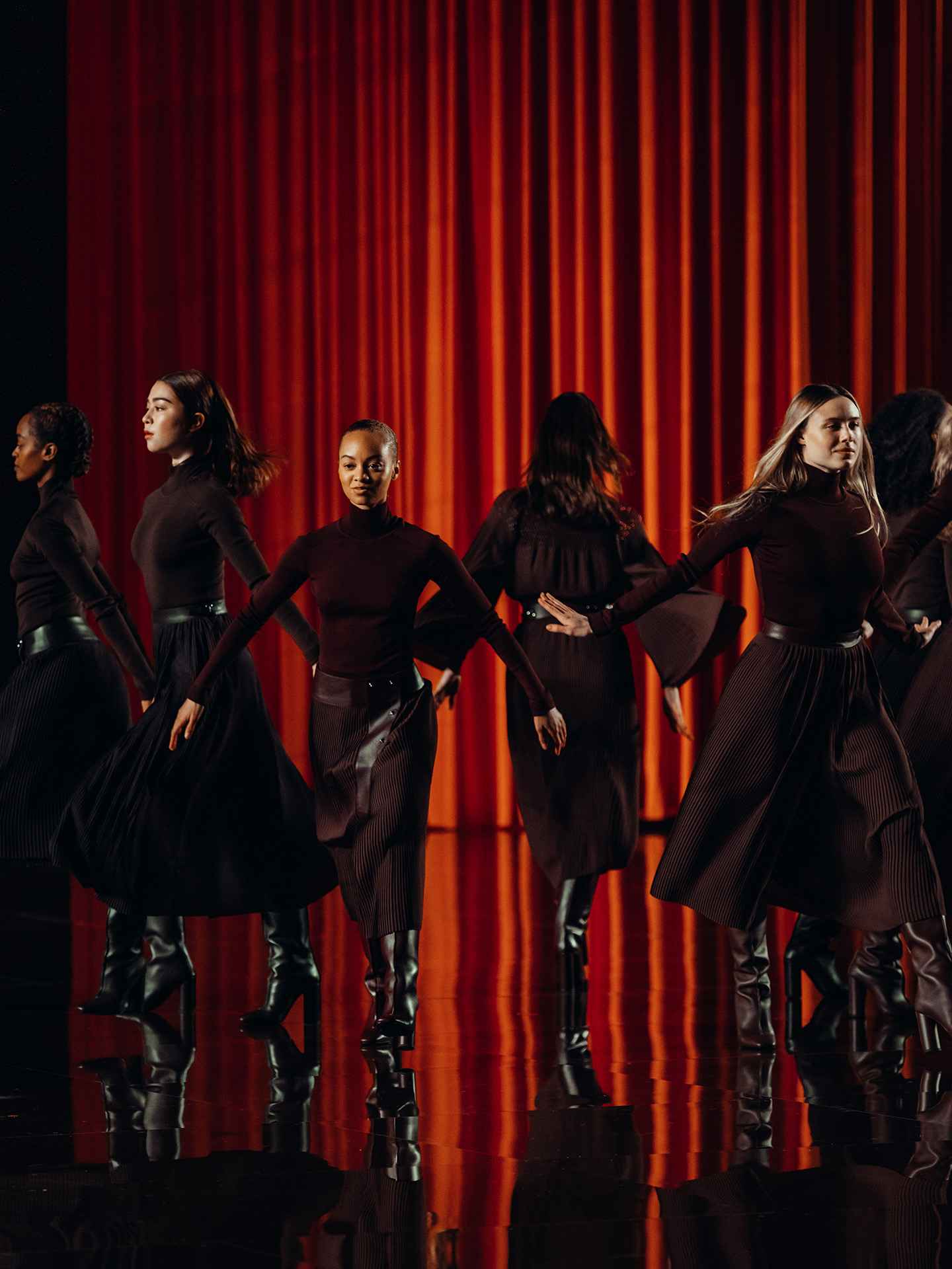 Dancers in maroon pleated skirts in front of an orange curtain, Hermès show in New York