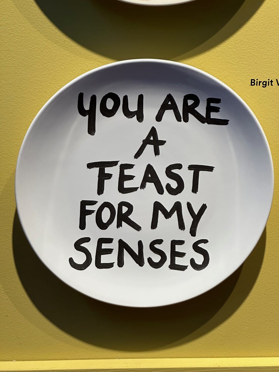 White plate hand-lettered “You are a feast for my senses” against a yellow wall