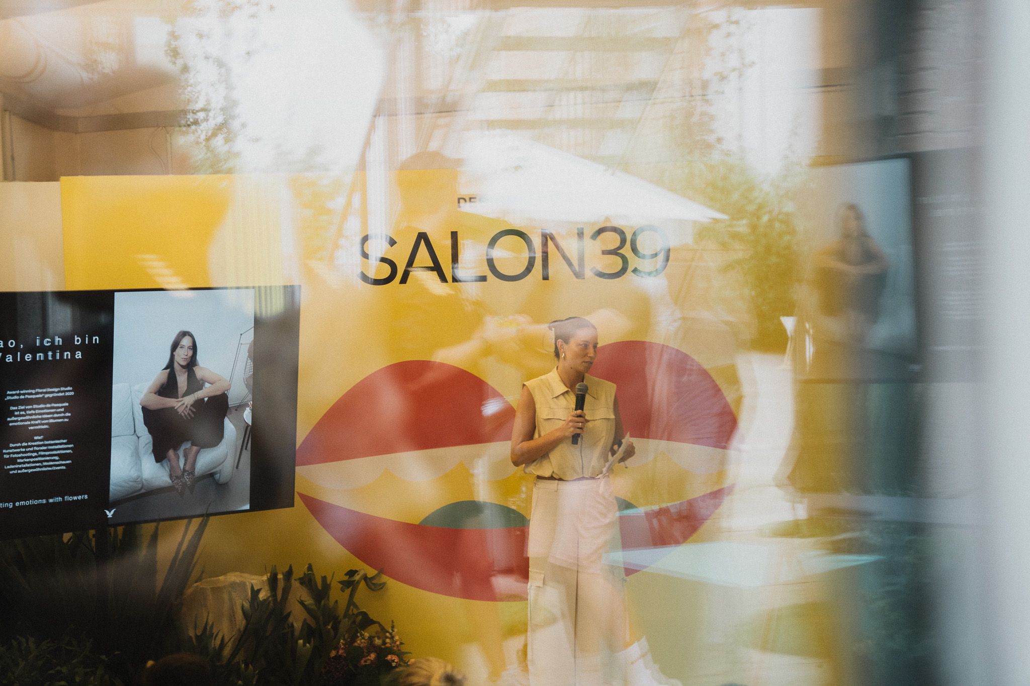 Durch Glas fotografierte Speakerin vor SALON39-Signage, mit Spiegelungen