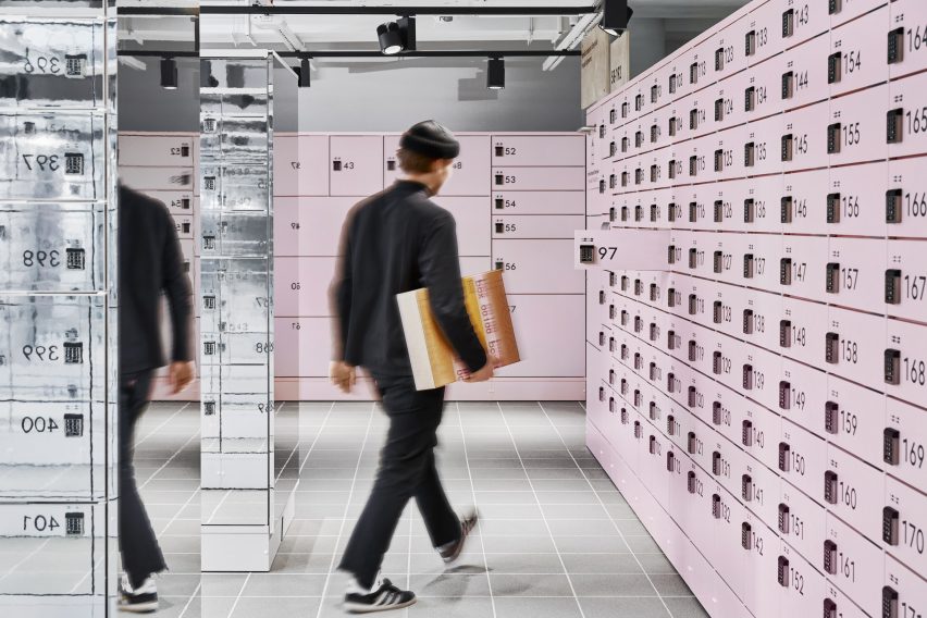 Person geht an einer Wand pinker Selbstbedienungs-Schließfacher mit Nummerierung vorbei.