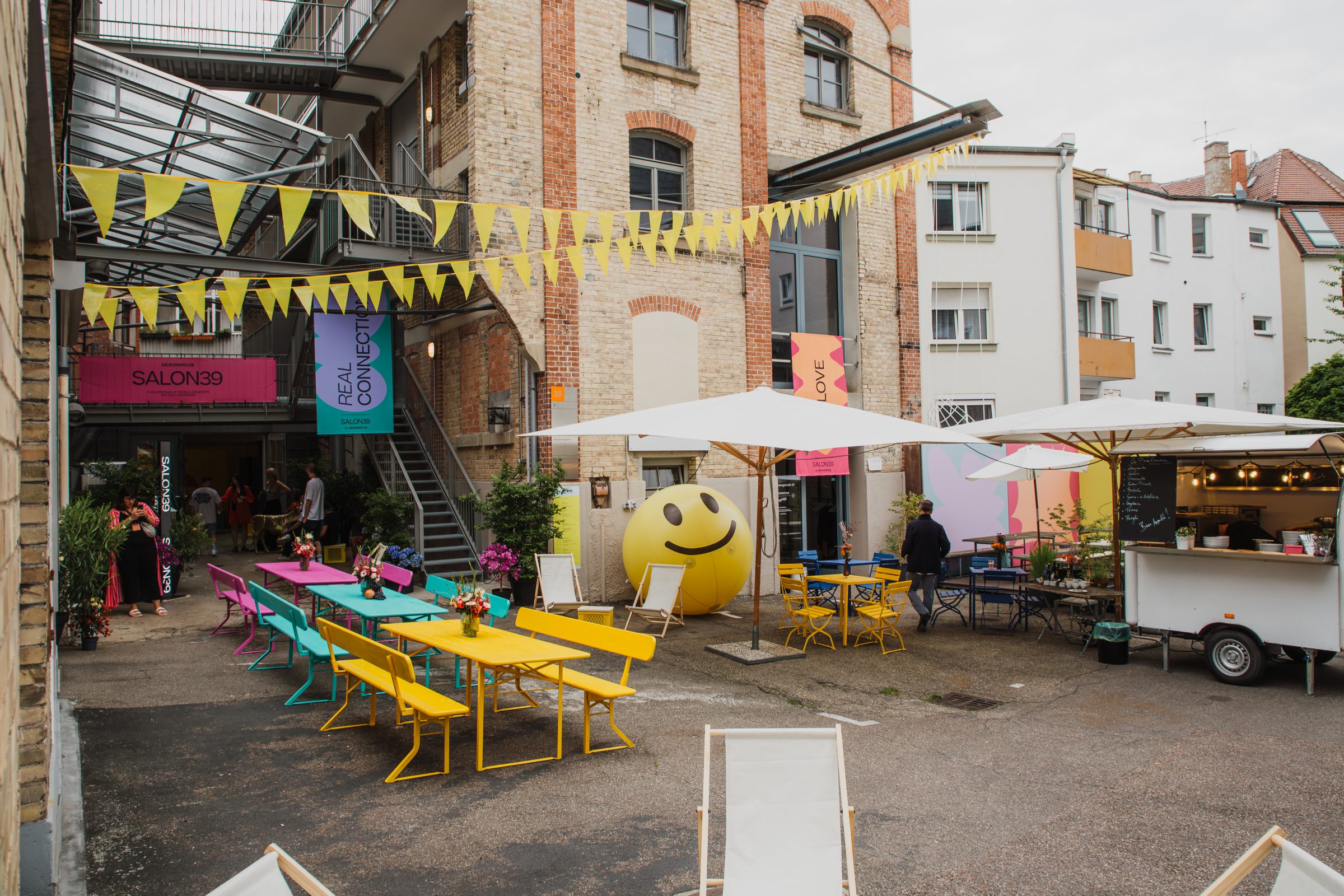 A colourfully decorated courtyard with benches, bunting and a food truck at the Salon39 event.
