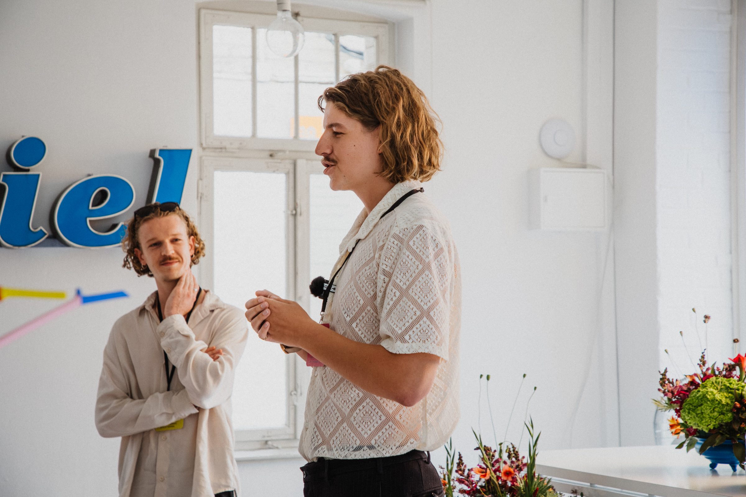 Two men talk in front of a neon sign and floral decor at Salon39.