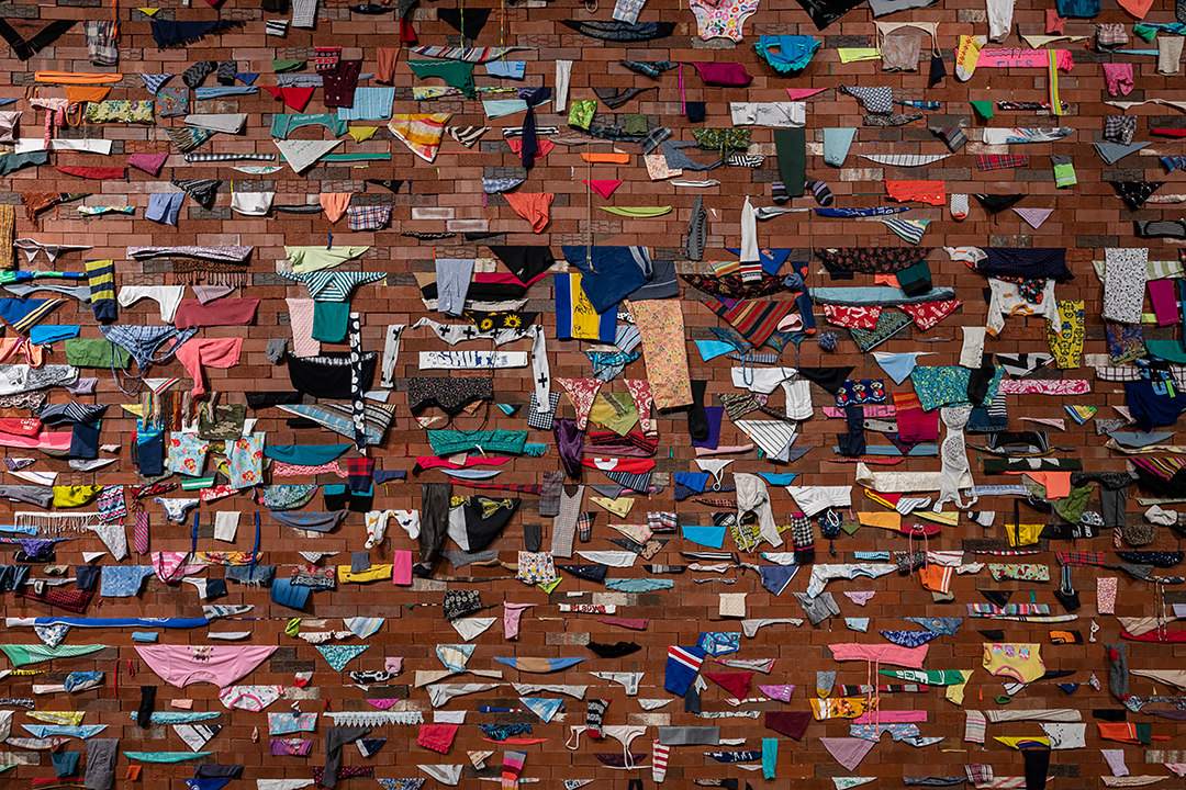 Nahaufnahme der Backsteinwand-Installation mit hunderten bunten Stoff- und Kleidungsfragmenten