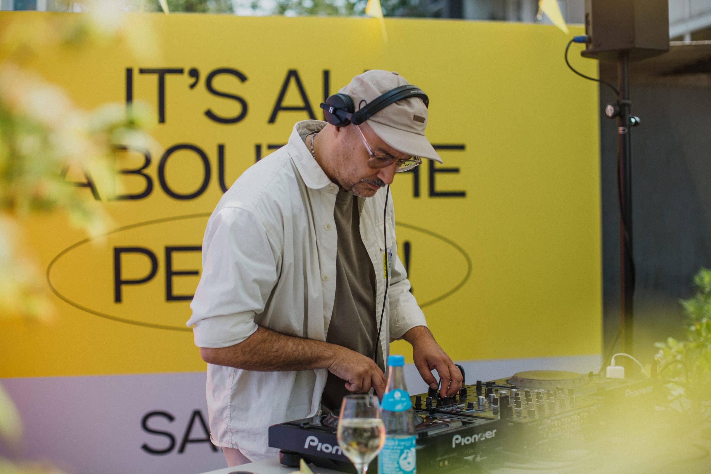 DJ mit Kopfhörern am Pioneer-Mischpult vor gelbem Banner „It's all about the people“