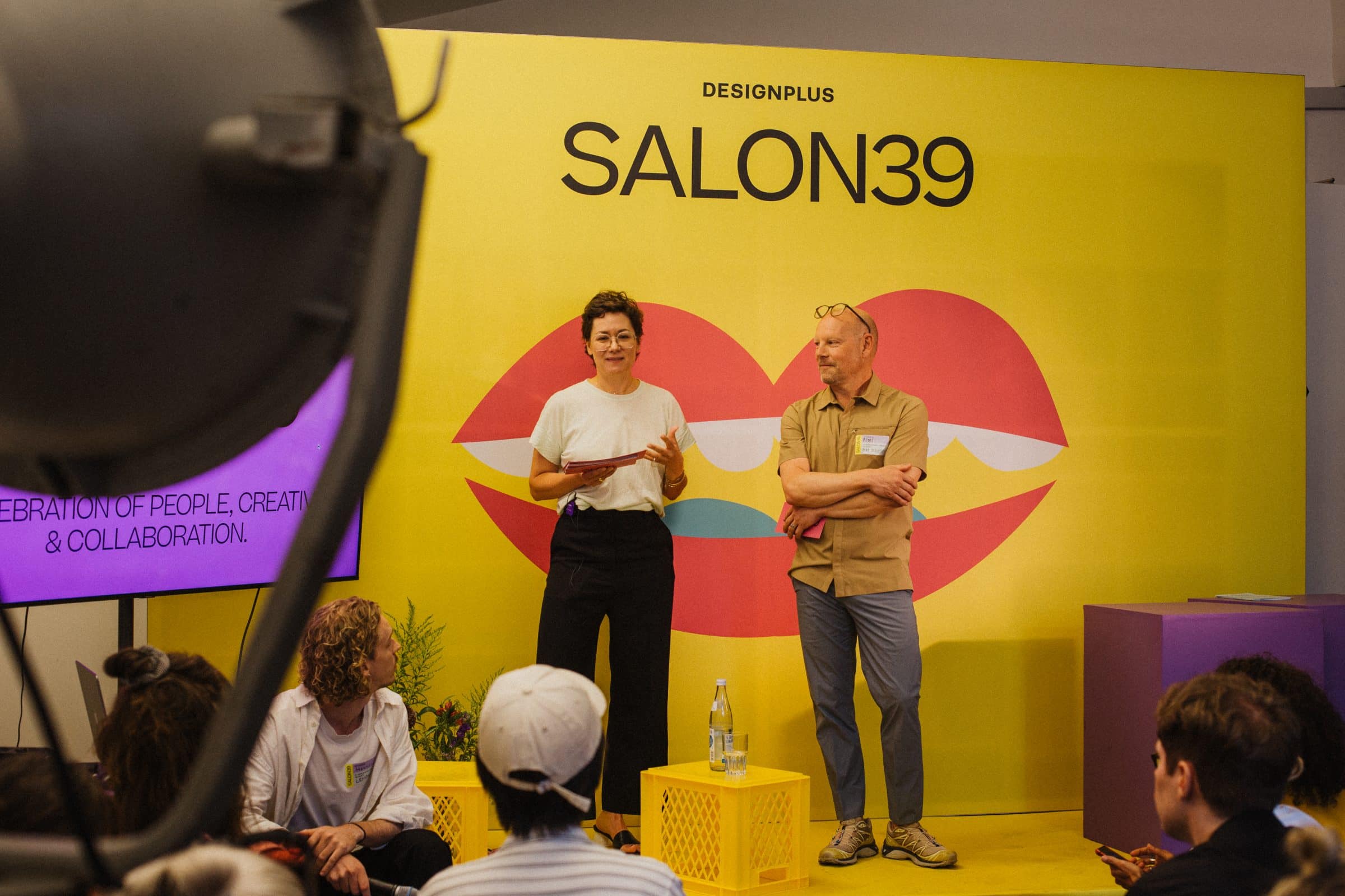 Zwei Speaker auf der Bühne vor dem gelben SALON39-Banner mit Lippen-Motiv
