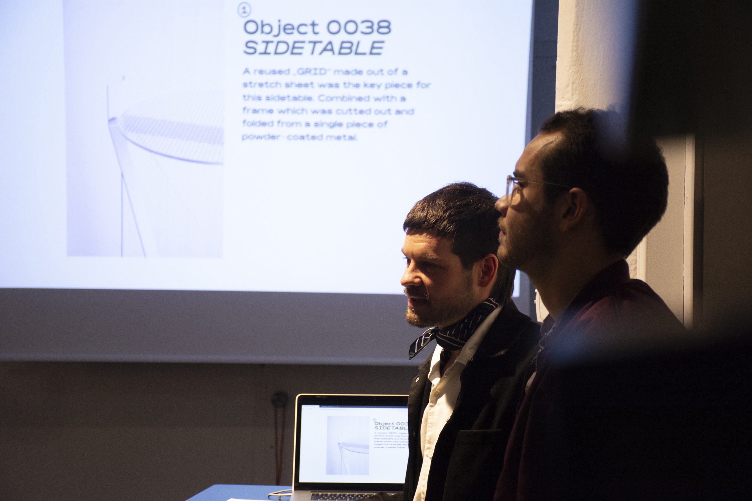 Zwei Männer betrachten die Objektbeschreibung „Object 0038 Sidetable“ bei der Second-Objects-Präsentation.