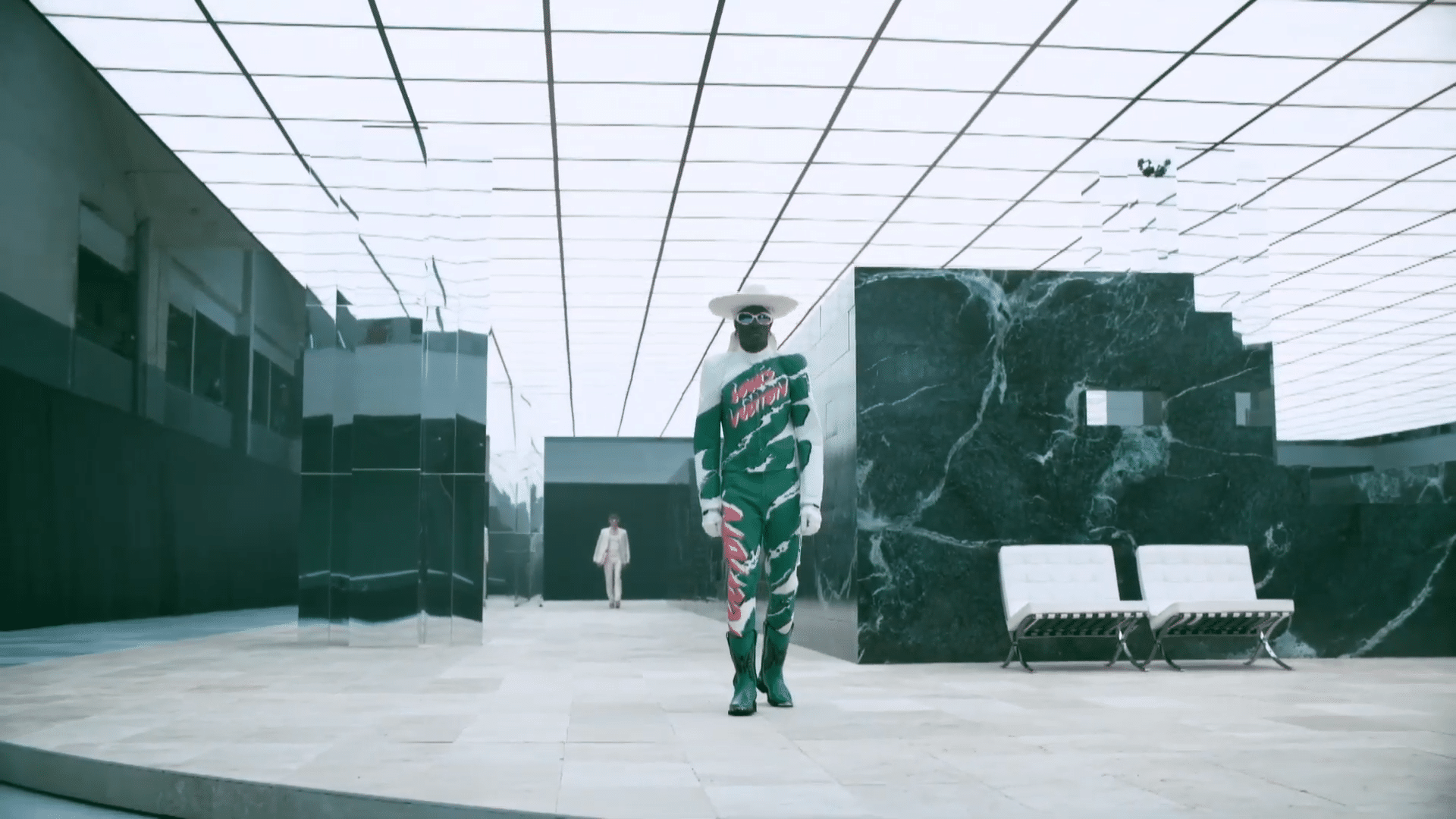 Model im camouflagefarbenen Louis-Vuitton-Look mit breitkrempigem Hut läuft durch die Marmorkulisse.