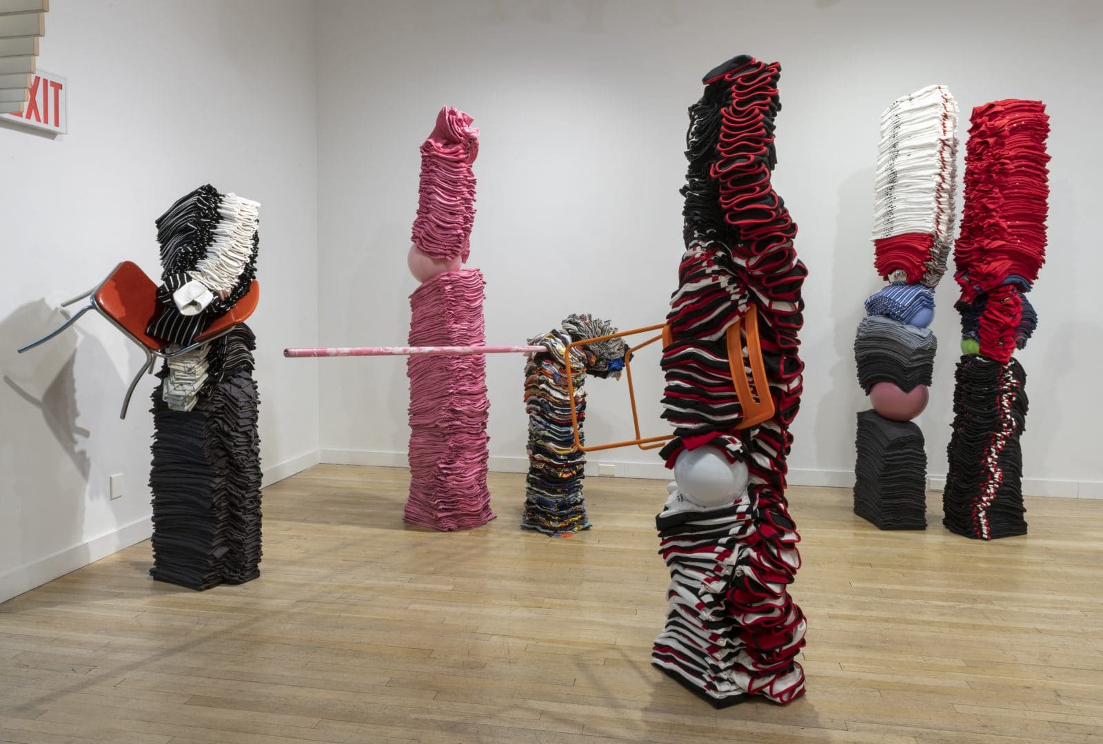 Installationsansicht mehrerer Textil-Skulpturen mit orangefarbenem Stuhl in der Galerie