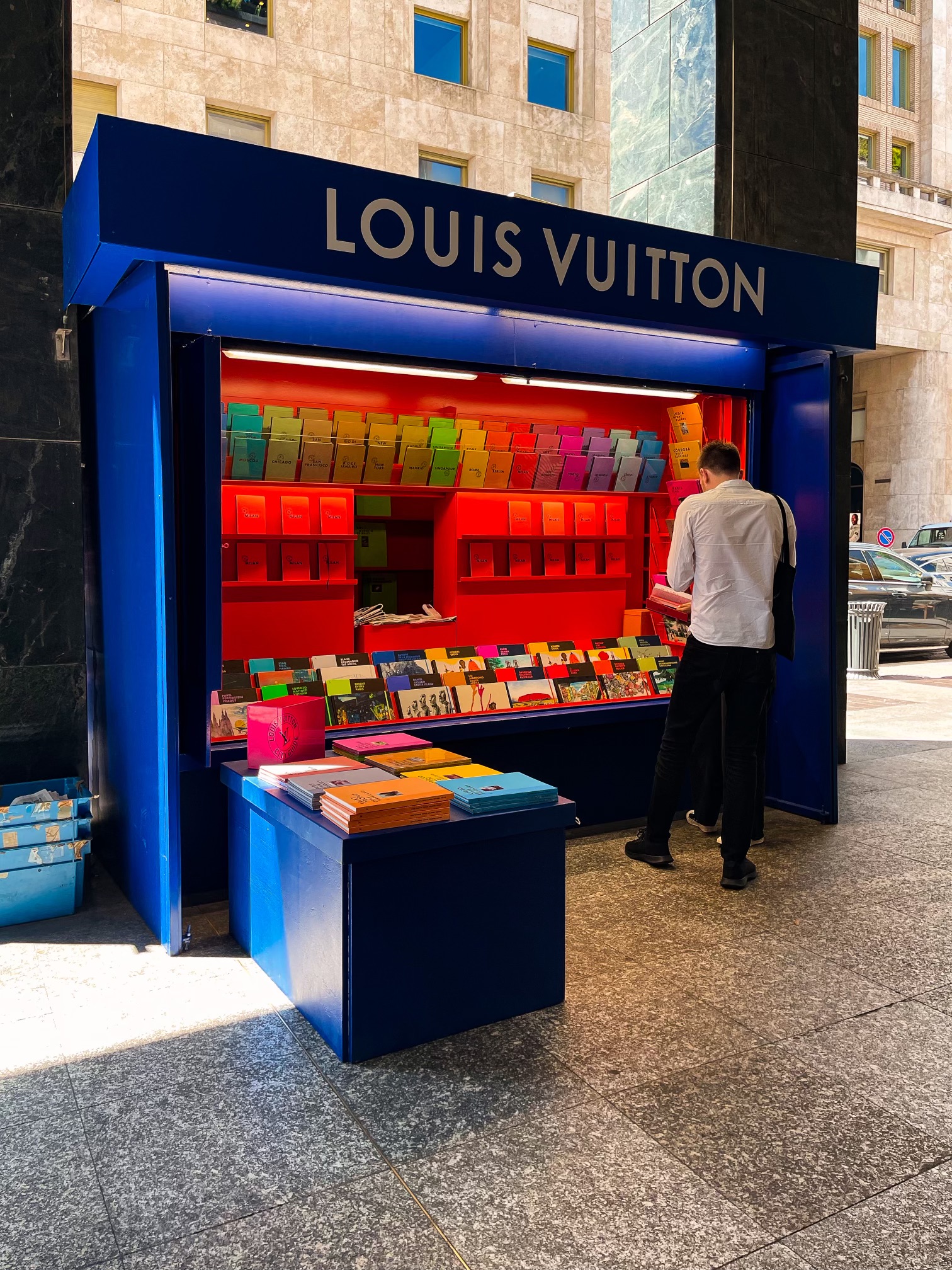 Blue Louis Vuitton newsstand kiosk on the street displaying colourful city guides, Milan