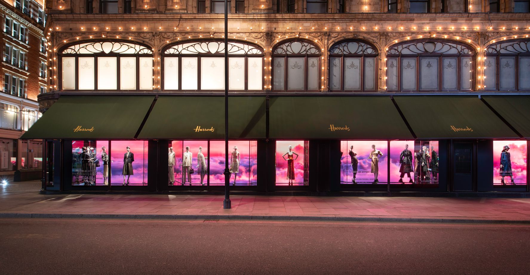 Harrods facade at night with a continuous row of pink Valentino window displays