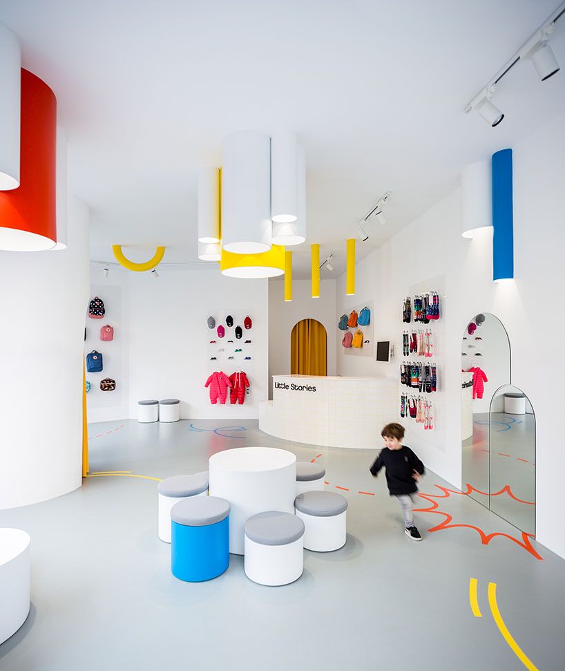 Kind läuft durch farbenfrohen Little-Stories-Store mit bunten Deckenleuchten und Hockern