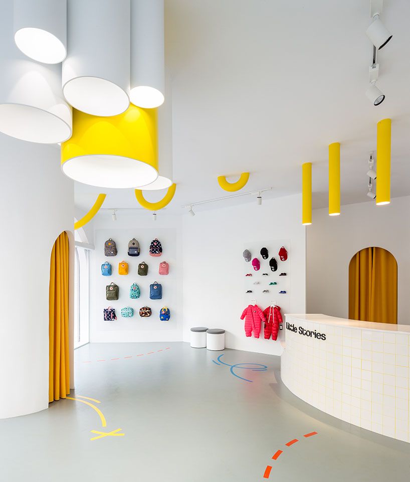 Little-Stories-Store mit gelbem Vorhang-Torbogen und Wanddisplays für Rucksäcke und Mützen