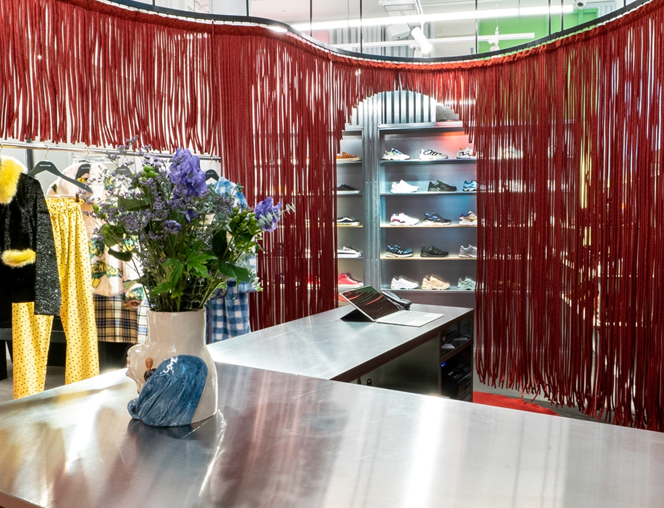 Roter Fransenvorhang umrahmt Tresen mit Sneaker-Regal und Blumenstrauß im Wood-Wood-Store