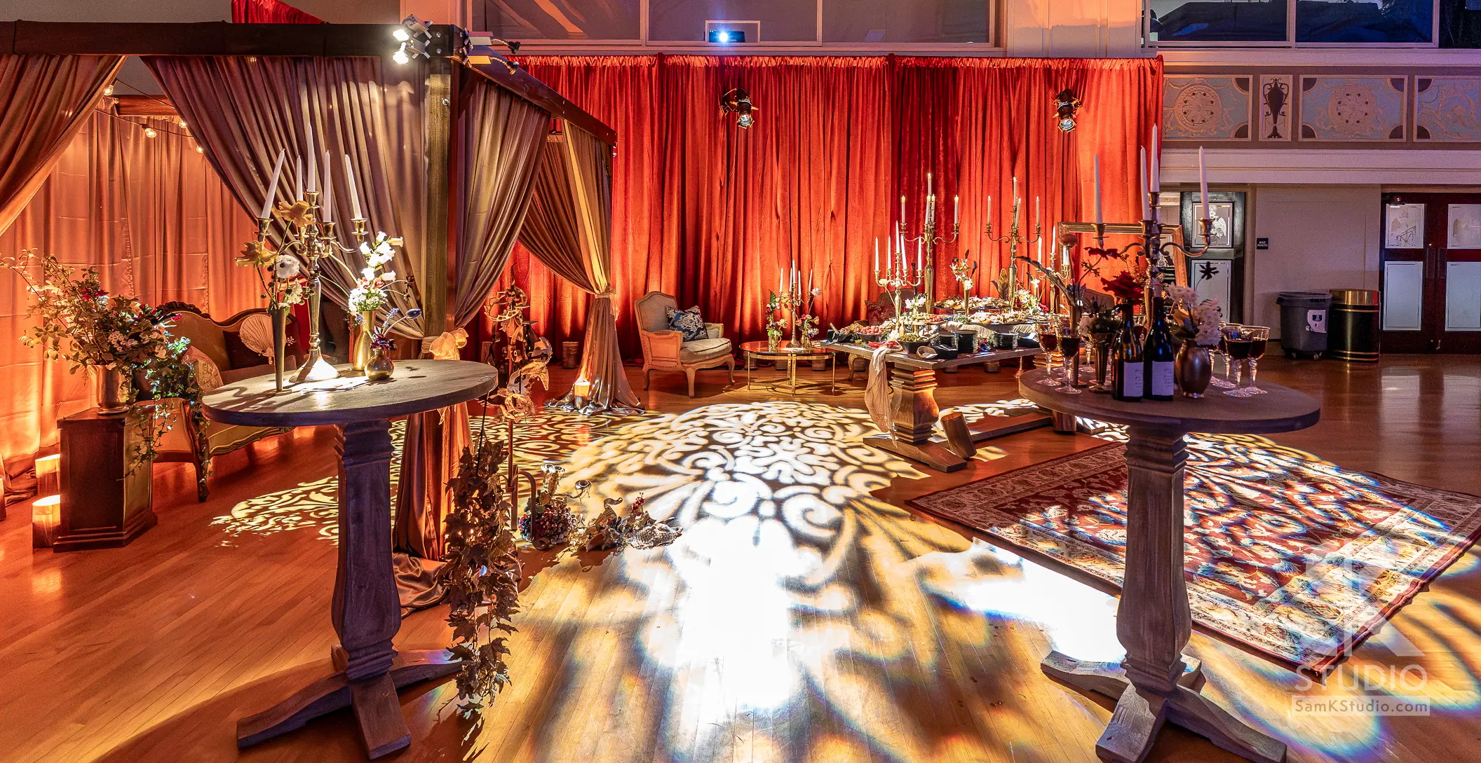 Event space with red drapery and a warm gold pattern wash on the floor, lit by Airsun Productions
