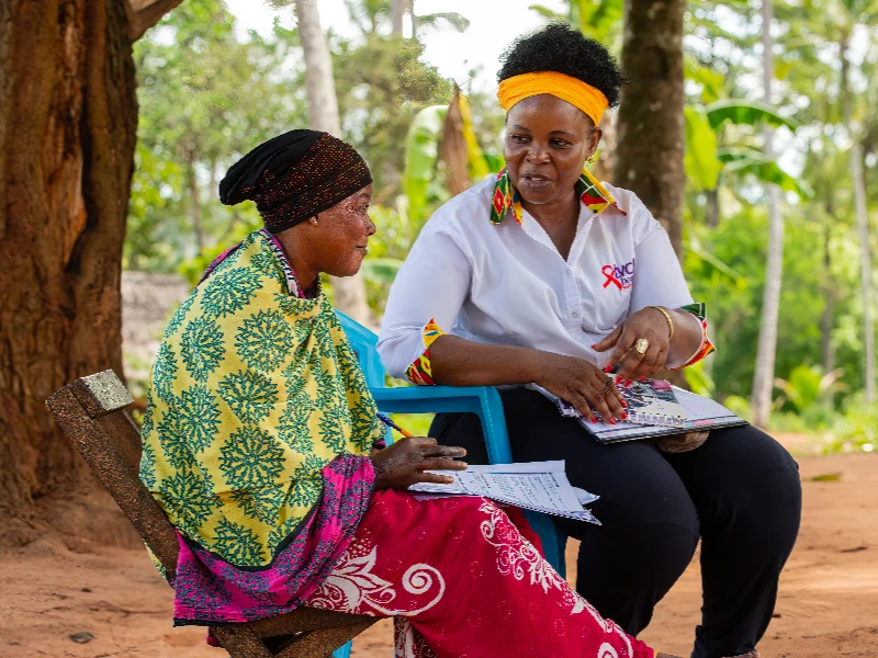 Photo of a community health worker speaking to a woman in a village in Kenya.