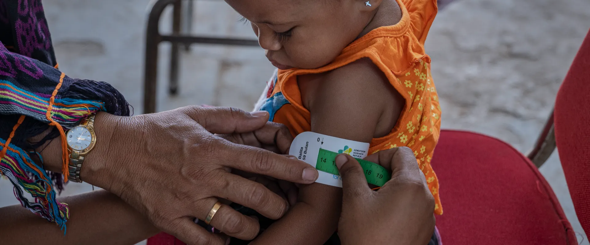 Photo of a mother measures the mid-upper arm circumference of her child to assess her nutrition status during a health and nutrition screening in Kupang City, Indonesia.