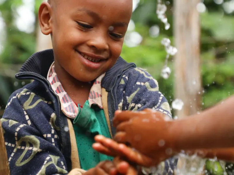 Photo of young child in Wolaita Zone, Ethiopia, enjoying fresh running water as part of the Geshiyaro Project on Water, Sanitation and Hygiene (WASH).