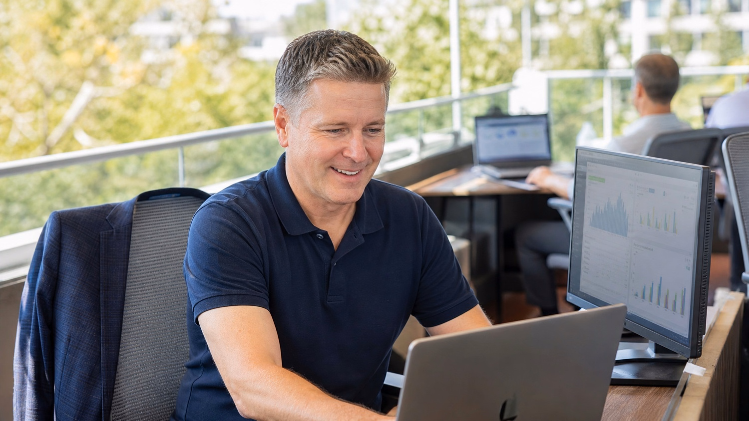 Man works on laptop on outdoor office terrace, jacket draped