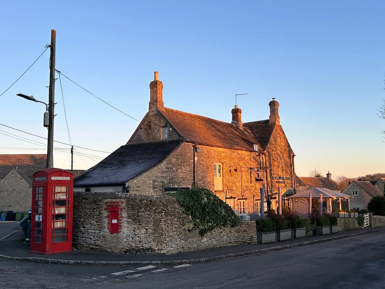 Pillar box red phone and post box next to the Keeper Arms, Quenington at sunset