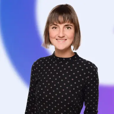 Smiling woman with short brown hair wearing a black patterned top in front of a blue and white background.