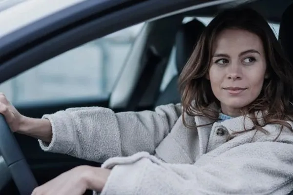 Young woman with long hair driving a car while looking ahead calmly.