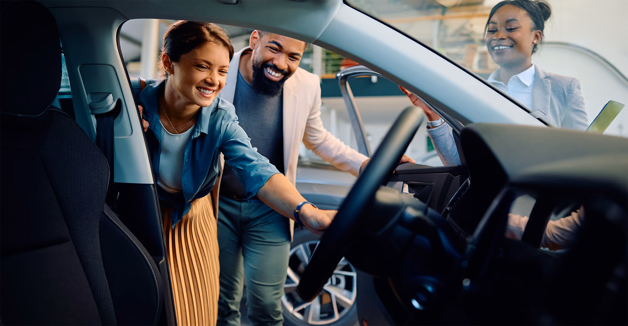Smiling couple inspecting the interior of a car while a salesperson stands nearby with a clipboard.