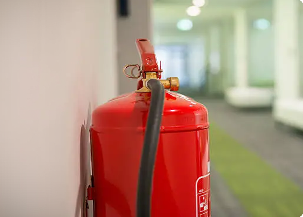 Close-up of a red fire extinguisher mounted on a white wall in a hallway with green and gray carpet.