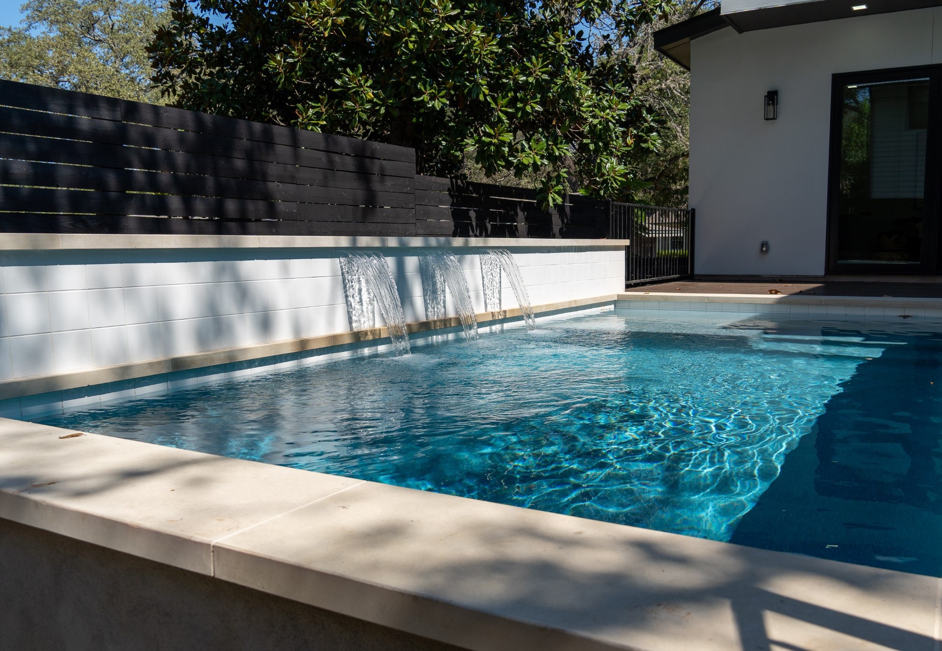 Custom build pool with turquoise water, modern white walls, and waterfall feature