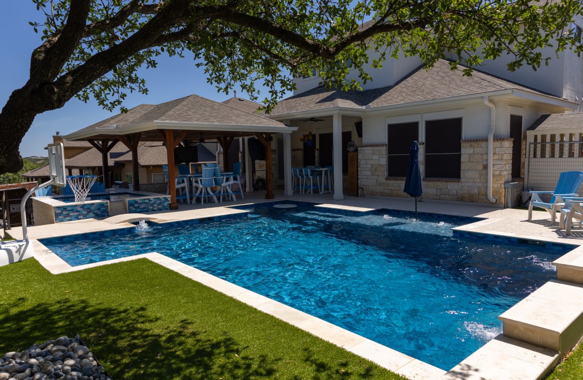 Custom built luxury pool with covered patio, lounge chairs, and stone home