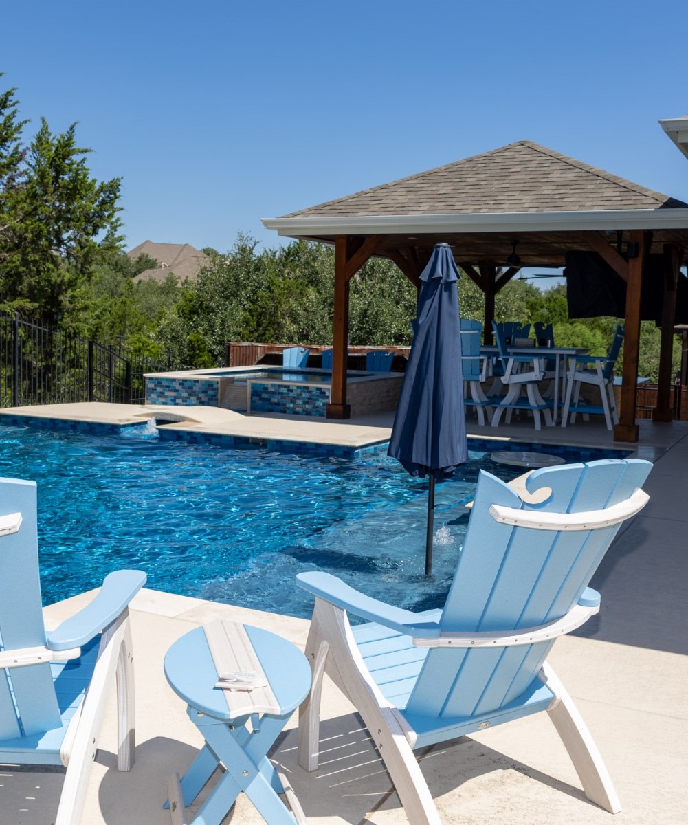 Custom backyard living space with pool, gazebo, and blue Adirondack chairs.
