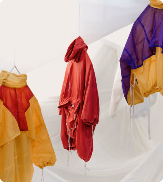 Red and yellow lightweight jackets hanging indoors on thin wires with a white fabric backdrop.