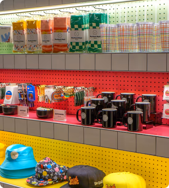 Store shelves with colorful socks, plastic cups, keychains, black mugs, and various hats displayed neatly.