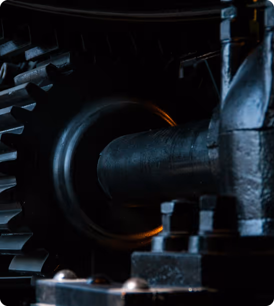 Close-up of dark metal gears and shaft in industrial machinery with low lighting.