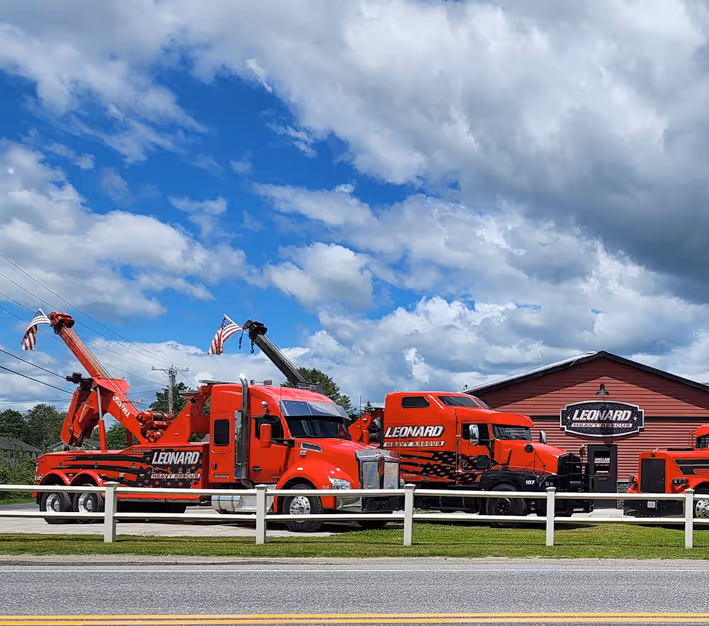 Red Leonard tow trucks parked in front of a Leonard building under a cloudy sky.